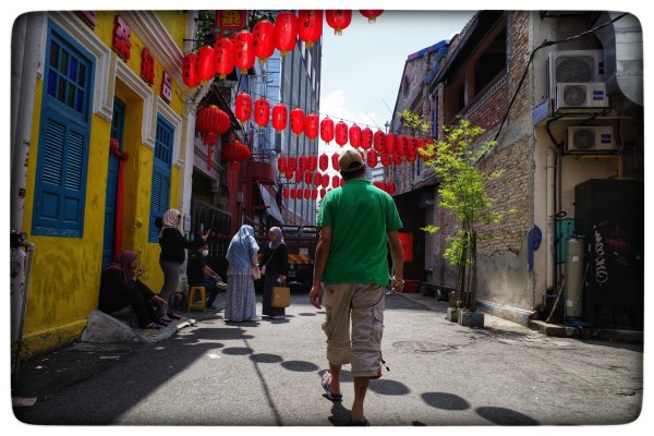 A man strolls down a street underneath a series of hanging red lamps